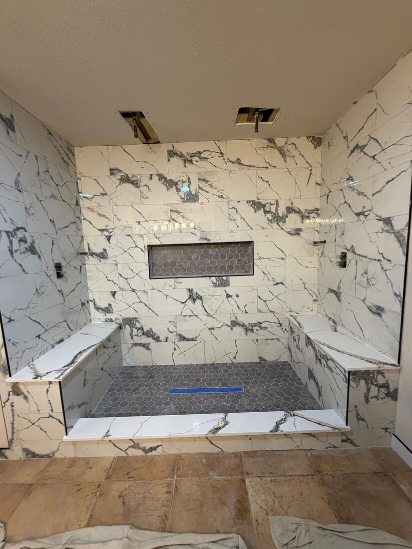 Full-stone shower with marble-look slab walls, built-in benches and a hex-tile niche