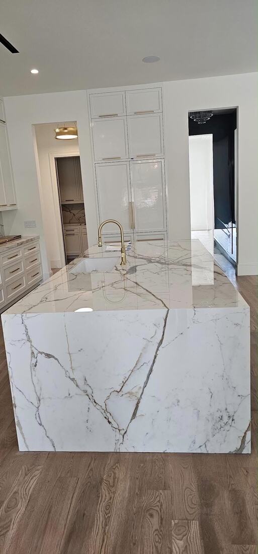 Full-height waterfall island in white marble-look stone with a brushed-gold faucet